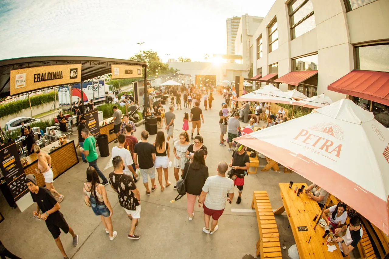 Evento de rua ao entardecer com barracas, mesas e grande público